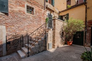 A narrow alley with a stone building, a metal staircase, and a potted plant.