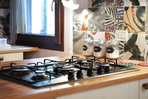 A kitchen with a gas stove, a window with curtains, and a wall with tropical leaf-patterned tiles.