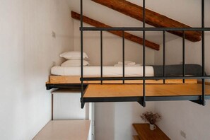 A bunk bed with a wooden headboard and a metal railing, a white wall, and a small plant on a wooden table. - Ca' del Majo (Venezia)