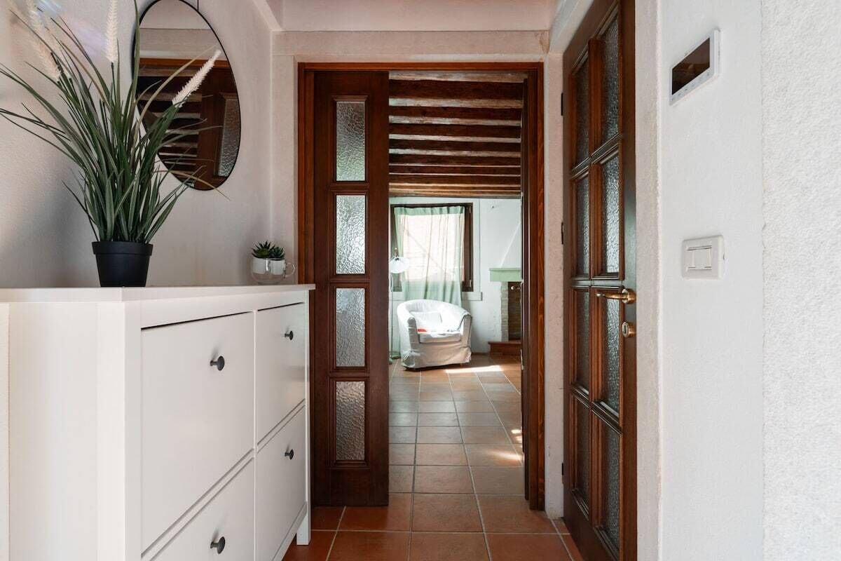 A hallway with a white dresser, a potted plant, and a door leading to a bathroom with a shower and a towel rack.