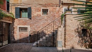 Une rue étroite avec un bâtiment en pierre, un escalier en métal et un portail.