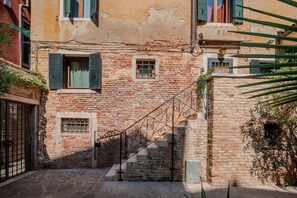 Una calle estrecha con un edificio de piedra, una escalera de metal y una verja.