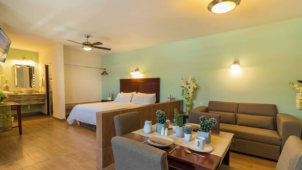 Habitación de hotel con cama, sofá, mesa de comedor con sillas, ventilador de techo y luces fijadas a la pared.