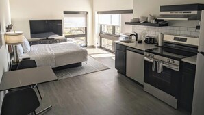 Quarto de hotel moderno com cama, escrivaninha, televisão e cozinha equipada com fogão, forno e pia.