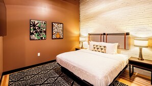 A hotel room with a large bed, two wall-mounted artworks, a brick wall, and a wooden ceiling.
