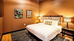 A hotel room with a large bed, two wall art pieces, a nightstand with a lamp, and a patterned rug. - One Bedroom King with views of the heart of downtown. (Madison)