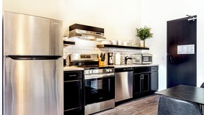 A modern kitchen with stainless steel appliances, a microwave, and a black dining table. - Studio Queen in the heart of downtown. (Madison)