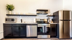 A modern kitchen with black cabinets, stainless steel appliances, a microwave, oven, dishwasher, and a refrigerator.