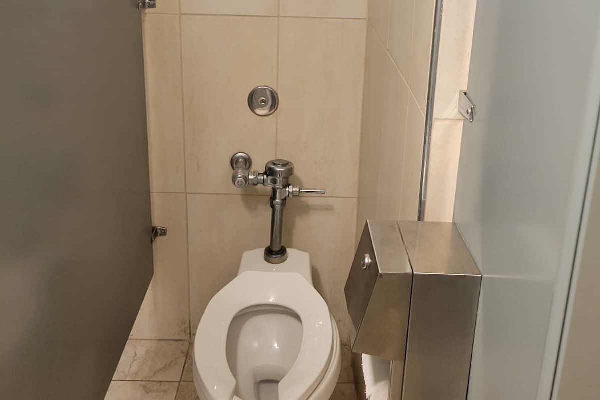 A bathroom with a white toilet, a metal bidet, and a small cabinet.