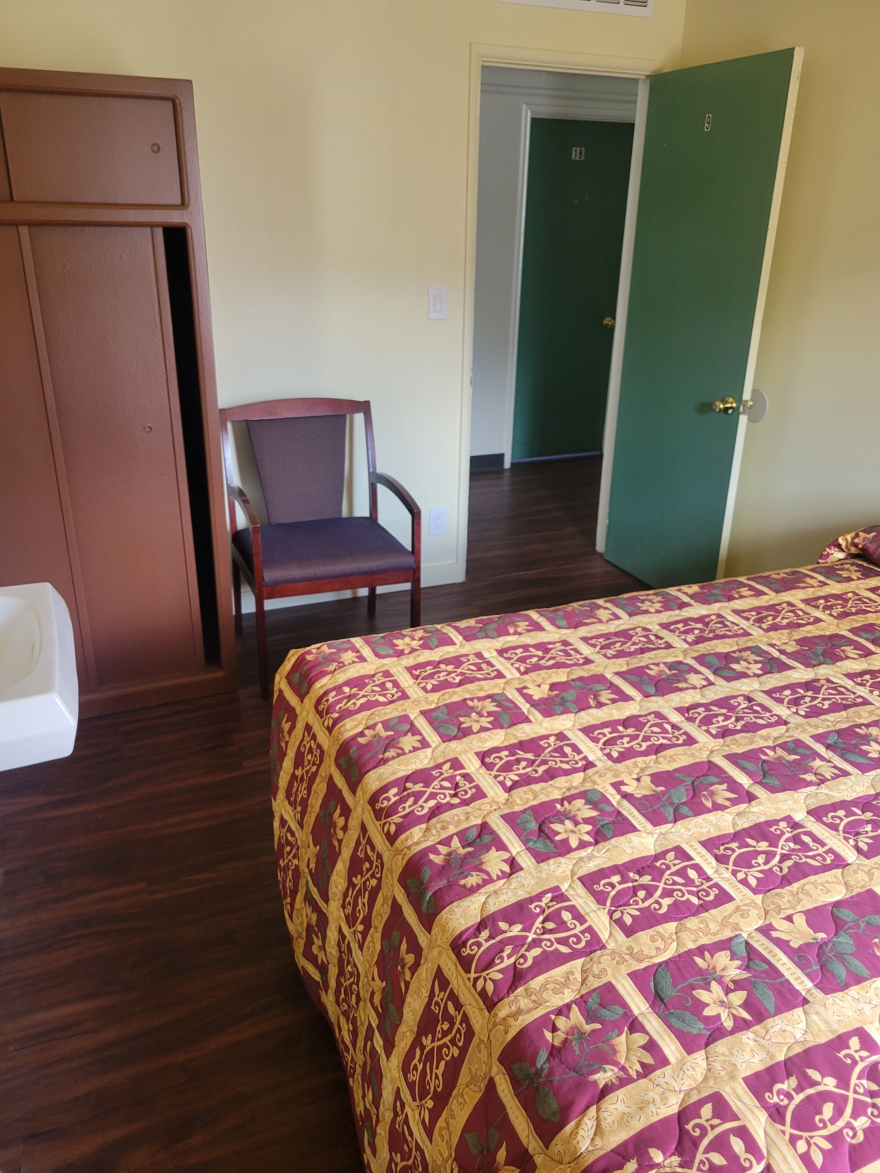 A hotel room with a bed, a chair, a wardrobe, and a green door.
