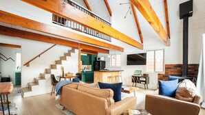 Amplia sala de estar con techo alto, vigas de madera, una escalera, una cocina y una chimenea.