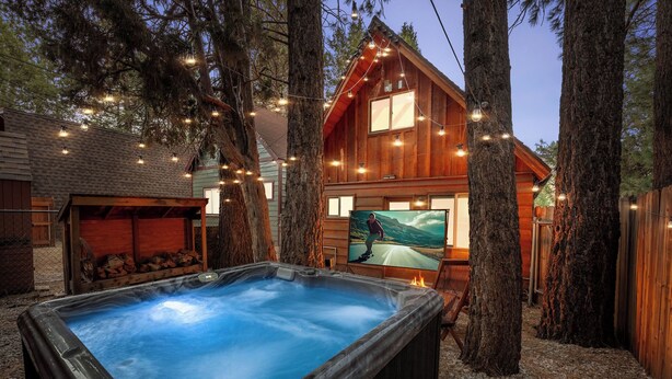 Una cabaña de madera con un jacuzzi, rodeada de árboles y luces colgantes.