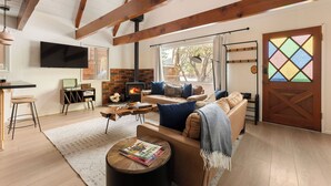 Una sala de estar acogedora con chimenea, vigas de madera, televisor y una puerta de vidrio emplomado de colores.