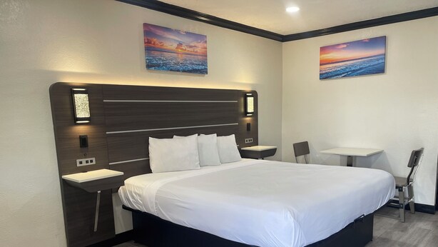 Een moderne hotelkamer met een groot bed, een nachtkastje, een stoel, een klein bureau en twee aan de muur gehangen schilderijen.