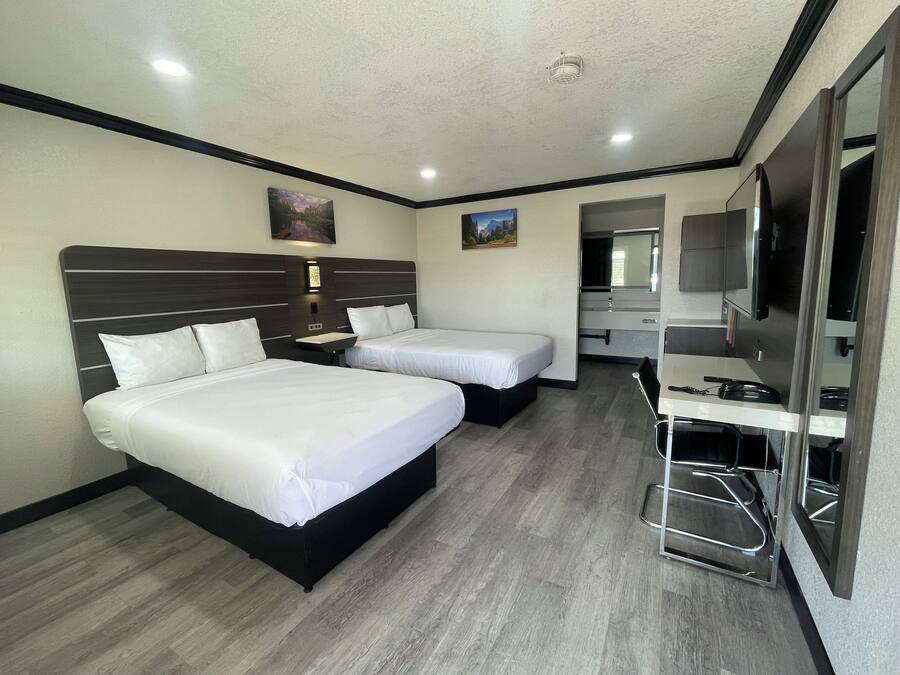 A hotel room with two beds, a desk, a mirror, and a TV.