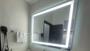 Een moderne badkamer met een grote spiegel, twee wastafels en een haardroger aan de muur.