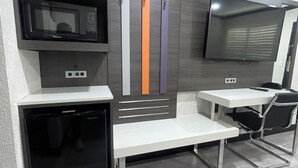 Een kitchenette met een magnetron, een kleine koelkast, een spoelbak en een flatscreen televisie aan de wand bevestigd.