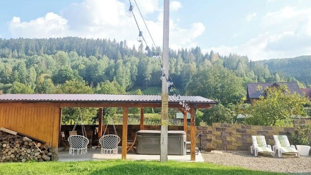 A wooden building with a covered patio, outdoor seating, and a hot tub.