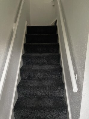 Stairs lead upwards through a residential space with a white handrail.