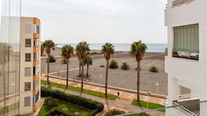 A view from a balcony overlooking a beach with palm trees, a road, and a building with balconies. - Blue Sea Modern Apartment with Sea View (Motril)