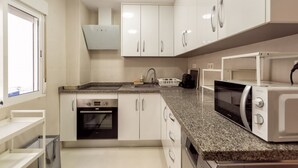 A modern kitchen with white cabinets, a built-in oven, a microwave, and a granite countertop. - Blue Sea Modern Apartment with Sea View (Motril)