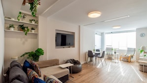 A modern living room with a sofa, a coffee table, and a TV. There are shelves with plants and a dining area with chairs. - Blue Sea Modern Apartment with Sea View (Motril)