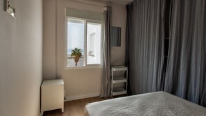 A bedroom with a bed, a window, a radiator, a shelf, and a curtain. - Blue Sea Modern Apartment with Sea View (Motril)