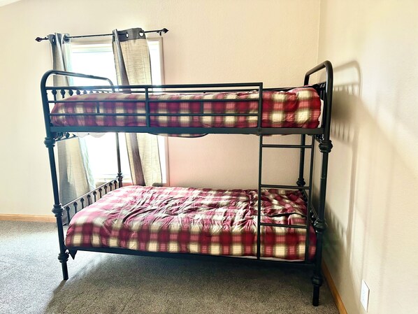 Una cama litera con una colcha escocesa, una ventana con cortinas y un piso alfombrado.