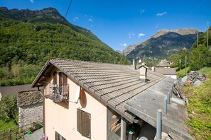 A mountain house with a sloped roof, stone walls, and a balcony overlooking a valley.