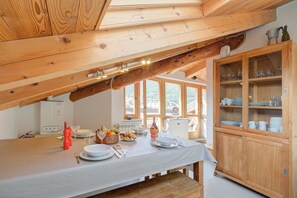 Una cucina con travi in legno, un tavolo da pranzo apparecchiato con piatti, bicchieri e una ciotola di frutta.