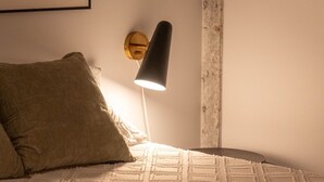 A bed with a textured white cover, a dark-colored pillow, and a black lamp on a wall. - Pleasure and Modernity: Dream Apartment for Rent in Saint-Roch, Quebec! (Québec)