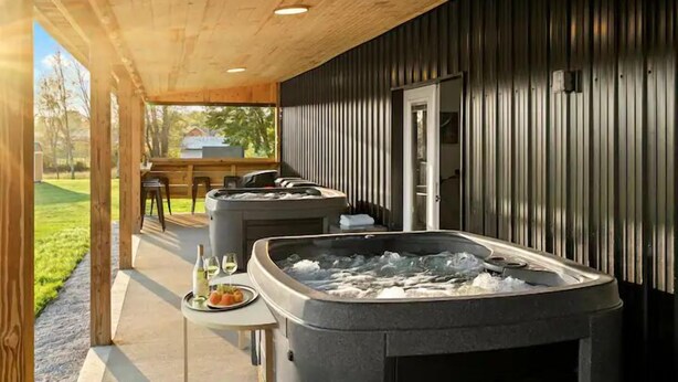 A covered outdoor area with hot tubs, a dining table, and a grill.