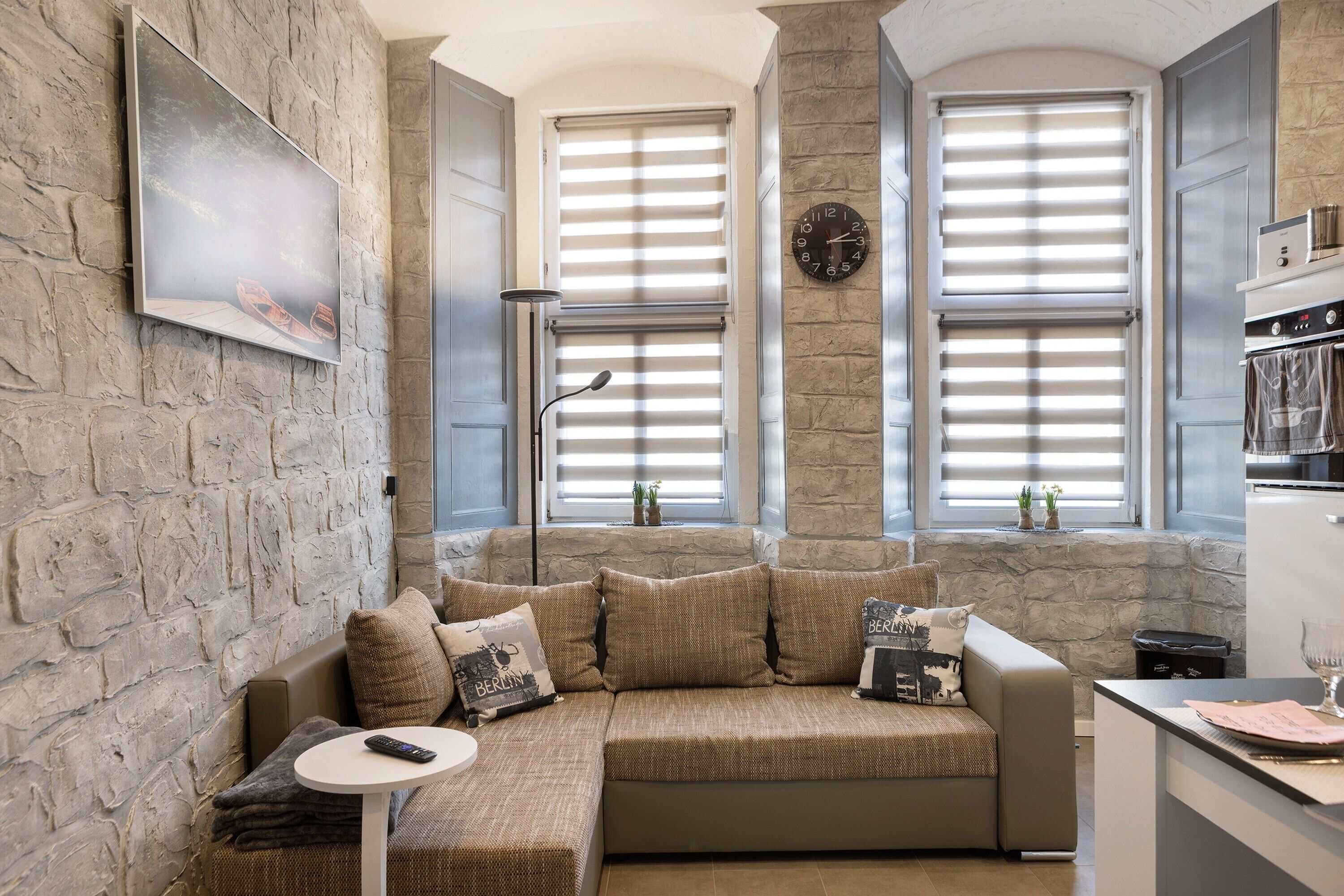 A cozy living area with a stone wall, a sofa with cushions, a small round table, and a clock on the wall.