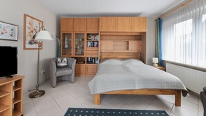 Een slaapkamer met een bed, een televisie, een boekenkast en een raam met gordijnen.