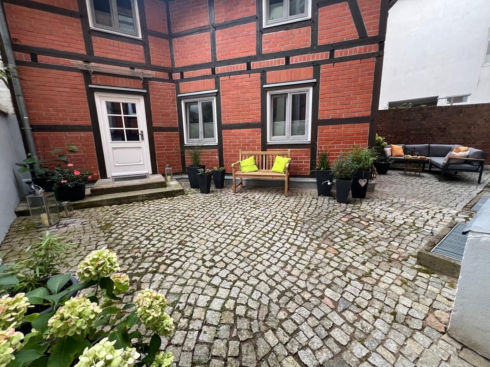 A courtyard with a cobblestone floor, a bench, potted plants, and a sofa.