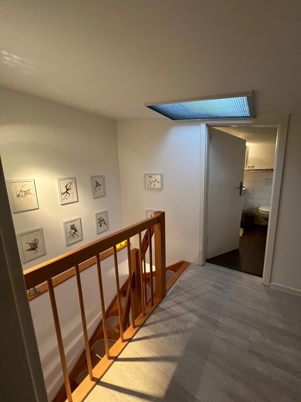 Eine Treppe mit Holzgeländern führt zu einem Raum mit weißen Wänden und einem Oberlicht.