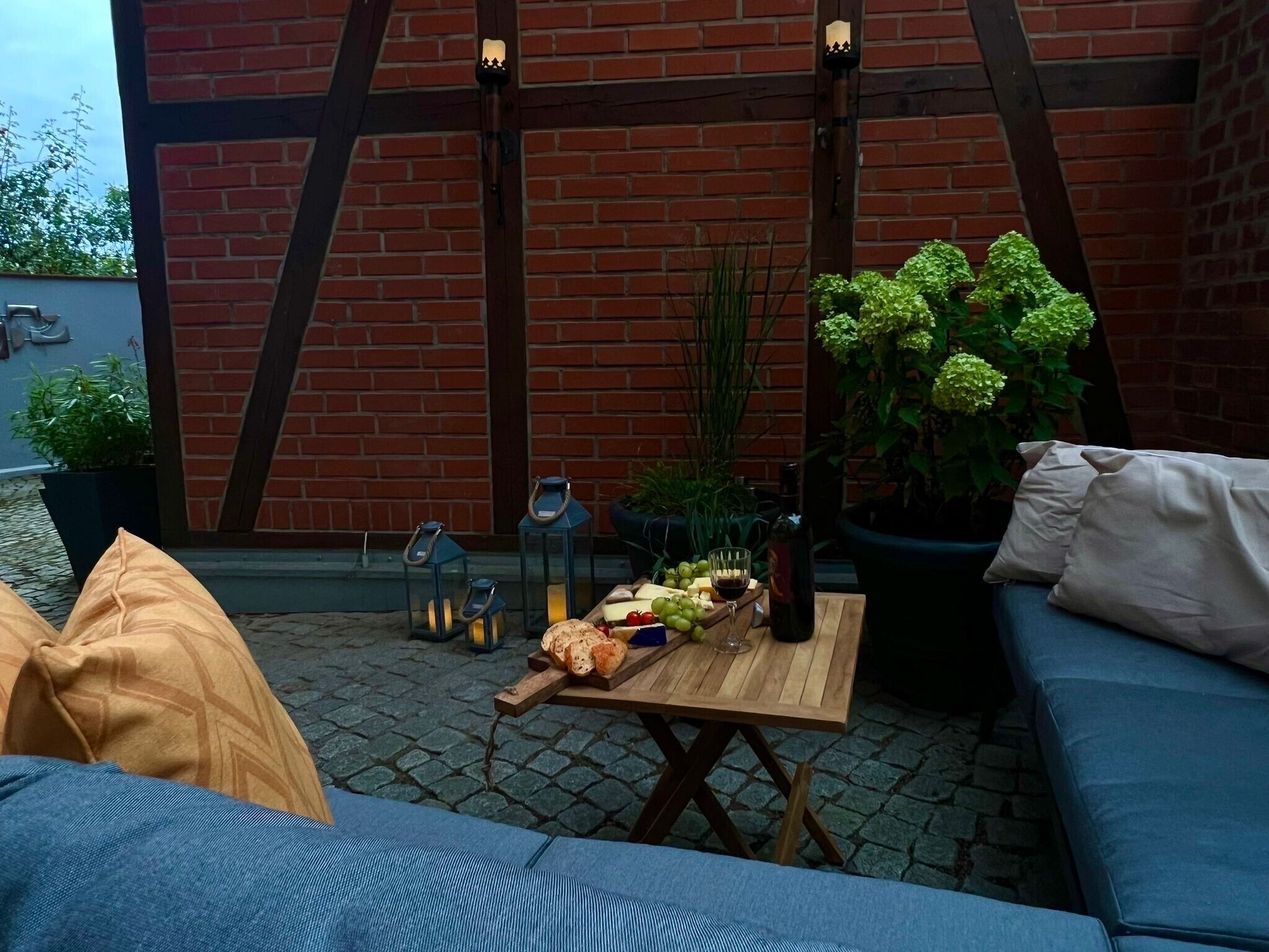 An outdoor seating area with a brick wall, a wooden table with food and drinks, and a blue sofa.