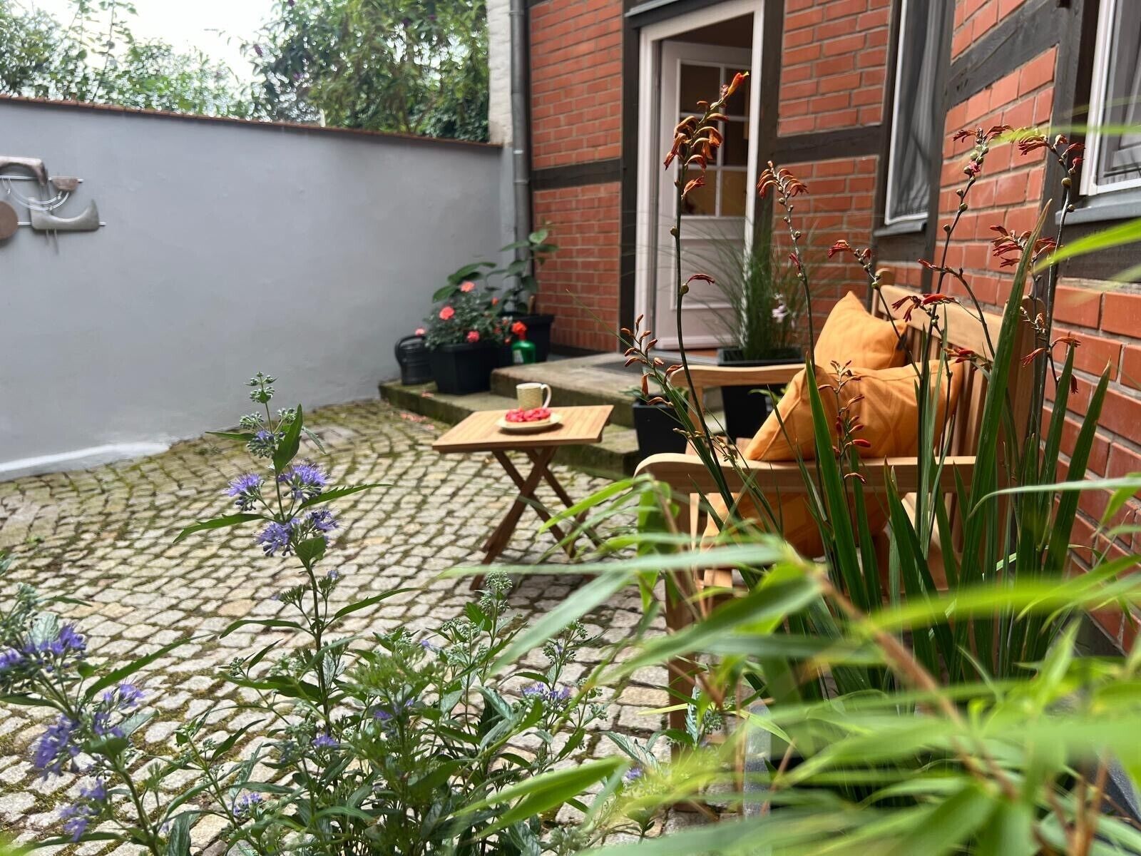Une terrasse avec un mur en briques, une table avec une chaise et des plantes en pot.