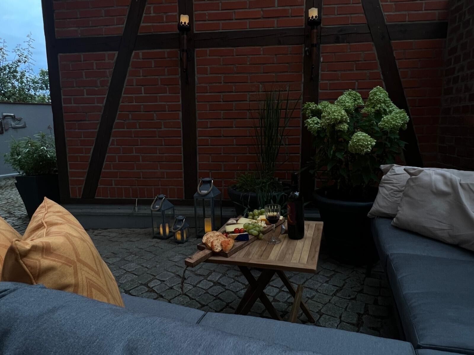 Un espace extérieur aménagé avec une table en bois, des coussins et un mur en briques.