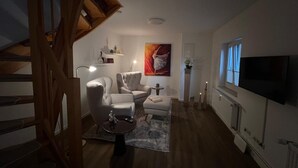 Olohuone, jossa on sohva, nojatuoleja, sohvapöytä, televisio ja taulu.