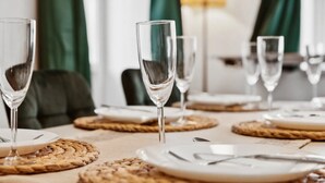 Una mesa dispuesta con vasos traslúcidos, platos y cubiertos, con individuales tejidos.
