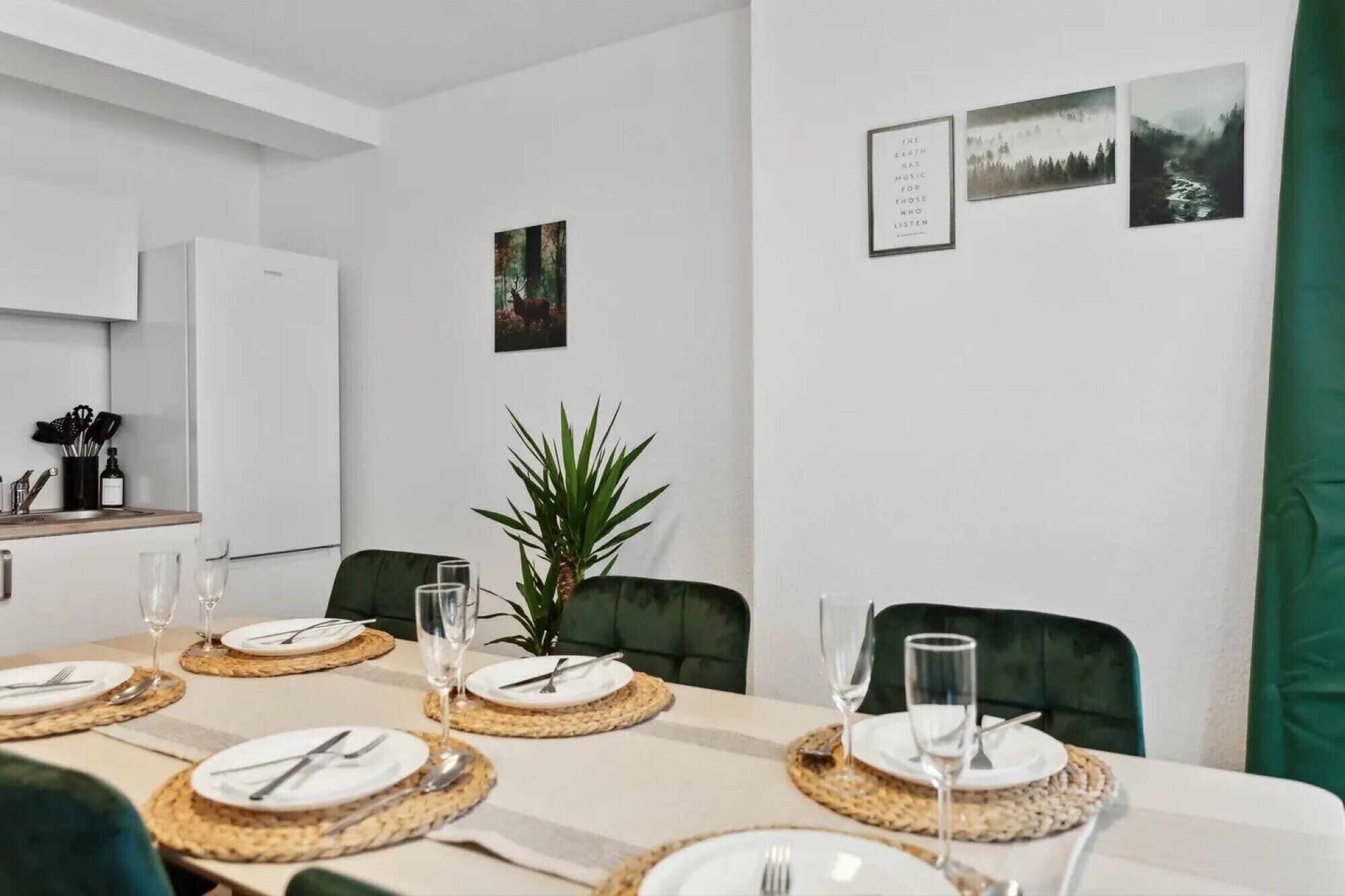 A dining area with a table set for four, a potted plant, and framed pictures on the wall.