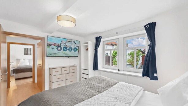 Un dormitorio con cama, cómoda, televisor y ventana con cortinas.