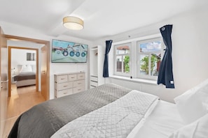 Une chambre à coucher avec un lit, une commode, un téléviseur et une fenêtre avec des rideaux.