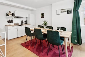 Une cuisine moderne avec des armoires blanches, un four encastré et une machine à café. On y trouve un coin repas avec une table dressée pour quatre personnes, entourée de chaises vert foncé.