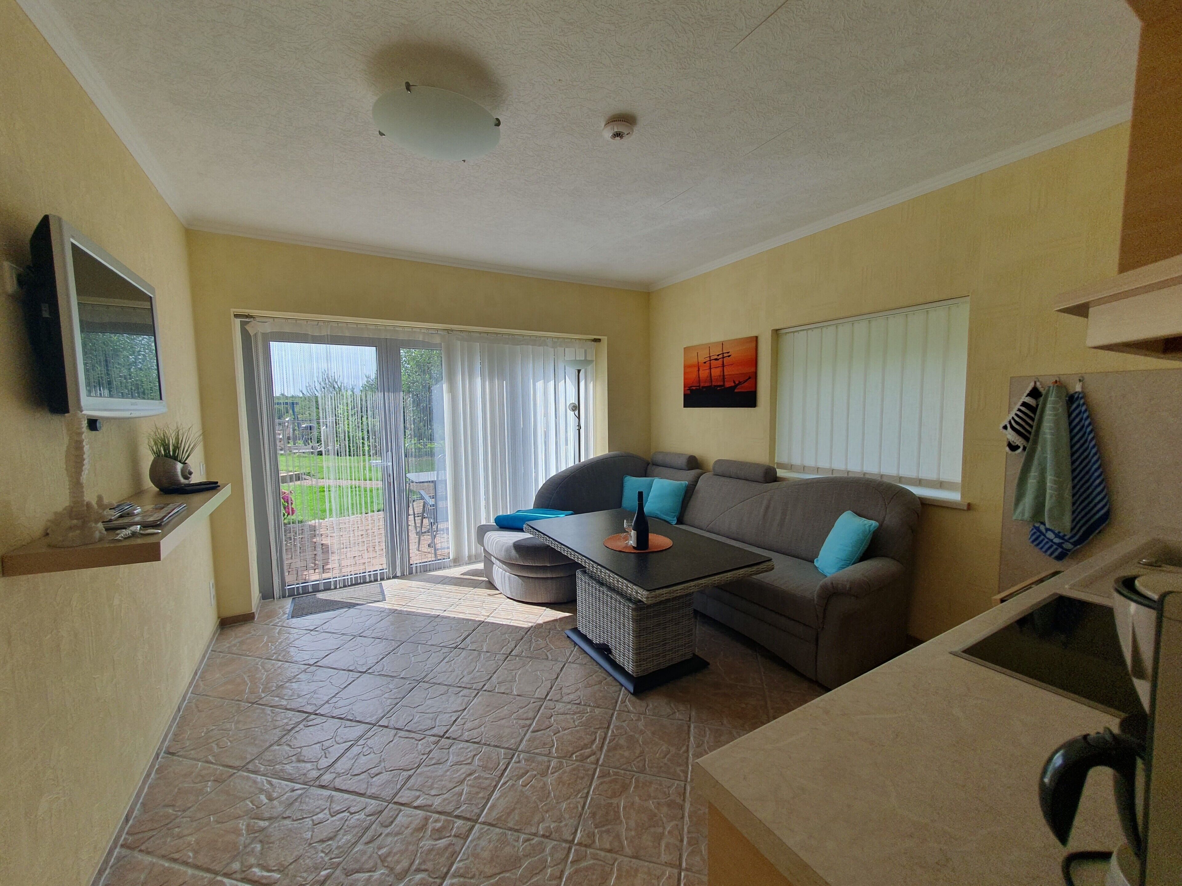A living room with a sofa, a coffee table, a TV mounted on the wall, and a sliding glass door leading to an outdoor area.
