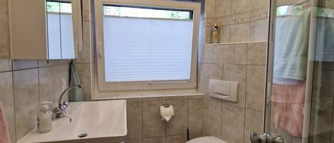 Un baño moderno con cabina de ducha de vidrio, inodoro, lavabo con espejo y ventana.