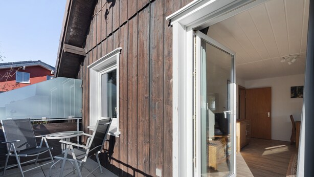 Patio esterno moderno con porta vetrata che dà su una stanza, parete esterna in legno e vista libera sull'edificio adiacente.