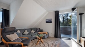 Un soggiorno moderno con divano, poltrona e tavolino, un tappeto decorato e vista attraverso una porta in vetro.