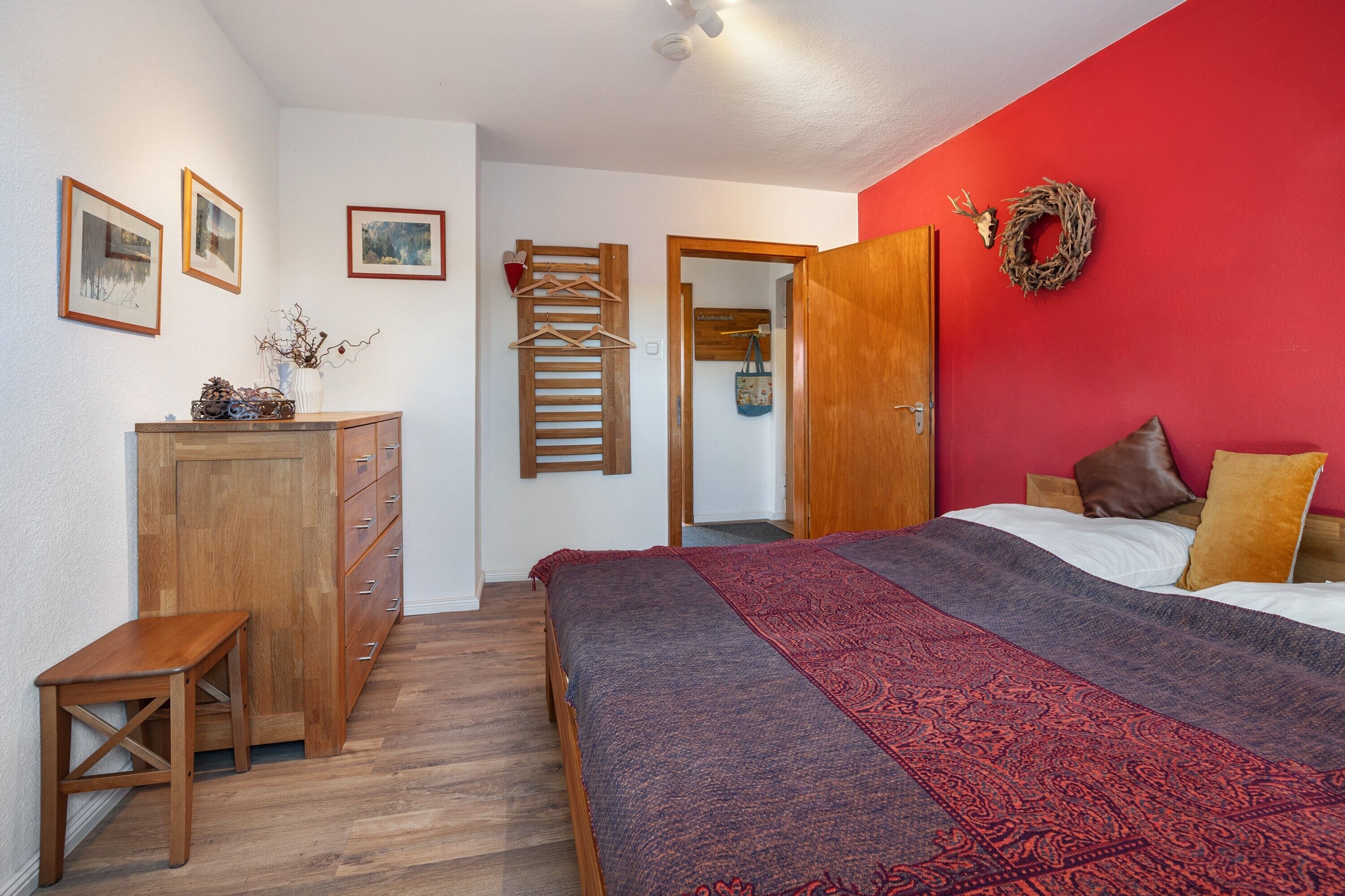 Un dormitorio con cama, cómoda de madera, banco, armario y pared roja.